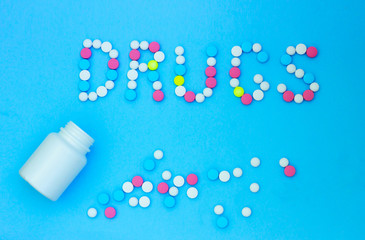 Pills on a blue background in the form of the word drugs