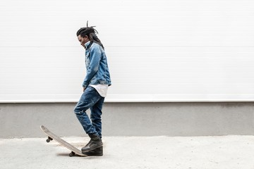 African guy with dreadlocks on a skateboard against a white wall