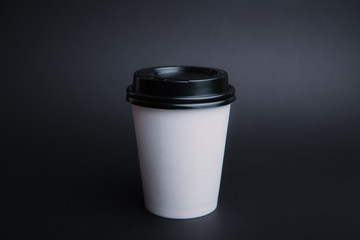Photo of a white take away cup with black lid over dark isolated background