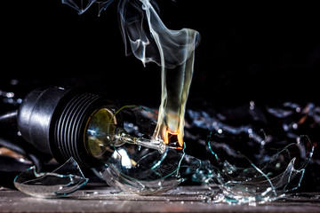 Amazing explosion of burning light bulb with splinters of broken glass and smoke on isolate black...