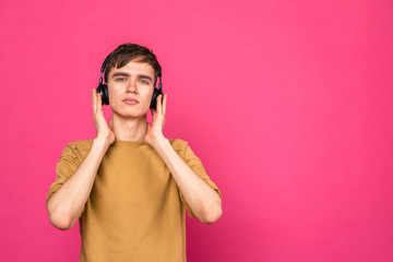 Fototapeta premium Young man standing with headphones on pink background