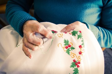 woman sewing cross stitch a tablecloth sitting at home