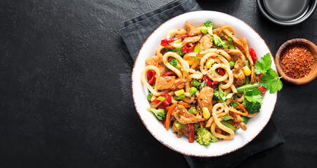 Udon stir fry noodles with pork meat and vegetables in a white plate on black stone background.