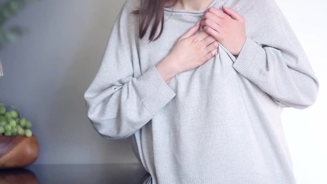 Beautiful female adult woman in grey cloth has acute pain in thoracic, heart attack or health issue. Massing chest and suffering from pain at kitchen. Heart health concept.