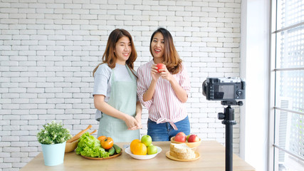 Two young asian women food bloggers talking while recording video with happy moment, vlog concept, people and technology communication