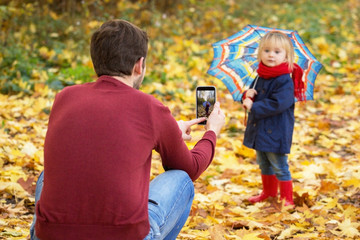 Father is making a selfie of his daughter in an autumn park.