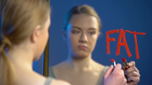 Young caucasian female writing word fat mirror glass, teenage anorexia disorder