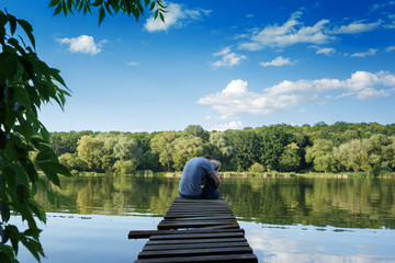 Obraz premium Dad and a tiny girl in dungarees relax at the river. Back view, copy space.