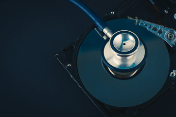 Data recovery or computer forensics concept, stethoscope dusty dismantle hard disk over dark background