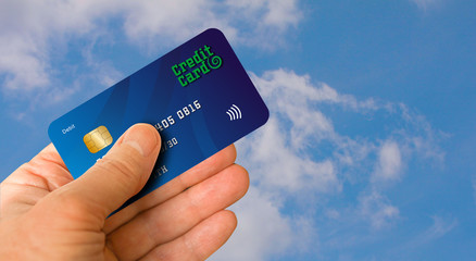 Hand holding credit card in the air against a blue sky. Travel concept.