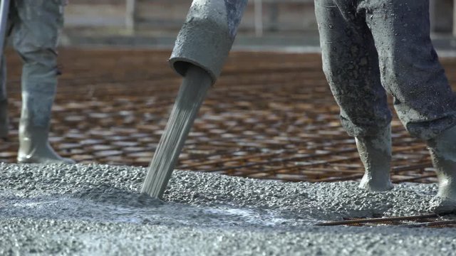 Workers concrete the foundation, rebar, pour cement mortar from pump concrete mixer. Concrete pump works on construction. Builders are building a factory, hangar, house
