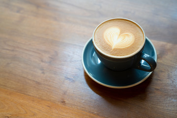 Top view of hot Coffee cup with a barista art heart shape foam on wooden table background with copy text space.