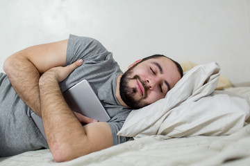 Young and beautiful man sleeps with a tablet in his arms.