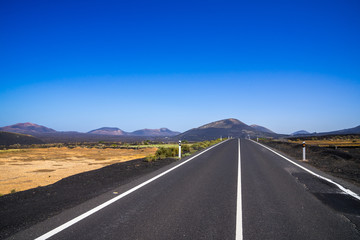 Spain, Lanzarote, Black asphalt road alongside pretty volcanic nature landscapes and volcanoes