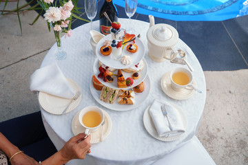 A woman sitting holding a teacup enjoying a high tea by a swimming pool