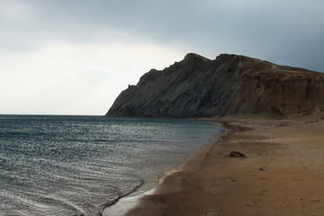 Fototapeta na wymiar Uninhabited sea shore. A mountain of clay is foreground.