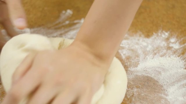 Man or woman chef's hands knead the pizza dough on the brown table close up selective focus 4K video.