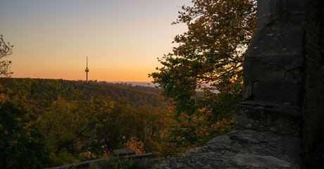 A television tower surrounded by a forest with a sunset sky in the background. Seen from the thick walls of castle Plesse in Lower Saxony, Germany.