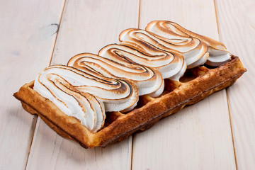 Belgian waffle with meringue. On a light wooden background