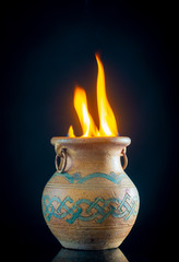 ire burning in ceramic pot with antique ornament on dark background 