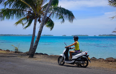 Young female tourist sitting on a scooter and observing the tropical nature. © helivideo