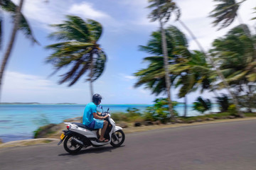 Young man speeds past the palm trees and exotic beaches on his motorcycle.