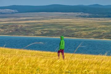 tourist girl walks in yellow grass across a field overlooking the water and mountains