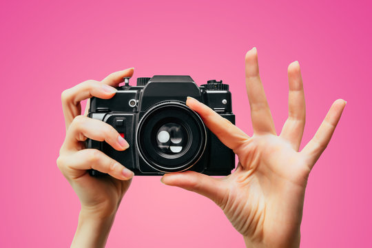 Vintage Camera in female hand. A photo. Photographer. Manual focus. Colored background. Pink