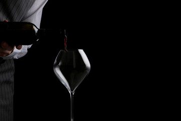 the waiter pours wine in glass on dark background