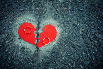 Divorce concept - broken heart with wedding rings on cracked asphalt. Toned