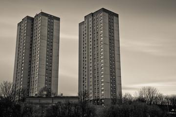A black and white shot of two towers of flats with a grey sky behind