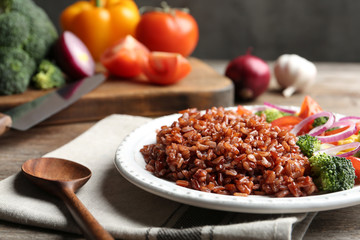 Plate of boiled brown rice with vegetables served on table, closeup. Space for text