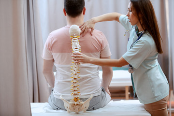 Young attractive female doctor holding spine model and truing to realize where is patient's painful...