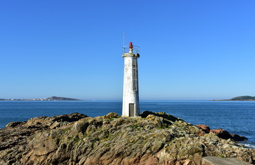 Old white lighthouse on the rocks with blue sea and sunny day. Galicia, Spain.