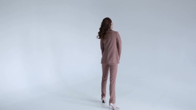 Business lady posing in a brown jacket and trousers on a white background. Sexy model with red hair goes forward, 50 frames per second