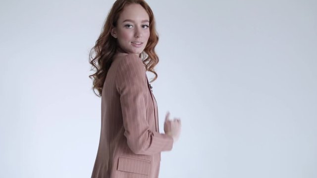 Business lady posing in a brown jacket and trousers on a white background. Sexy model with red hair goes forward, 50 frames per second