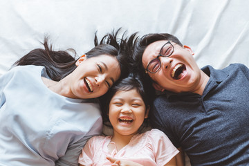 Happy Asian family laying on bed in bedroom with happy and smile, top view