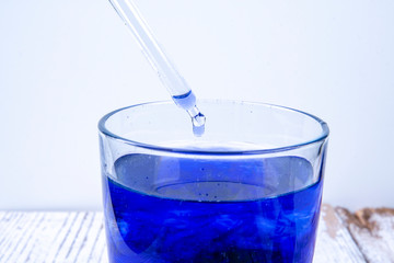 Pipette drips into a glass with blue liquid
