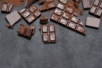 Dark or milk organic chocolate pieces and cocoa powder on dark concrete backgound
