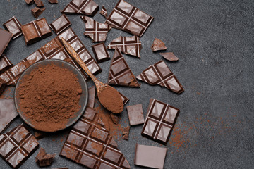 Dark or milk organic chocolate pieces and cocoa powder on dark concrete backgound