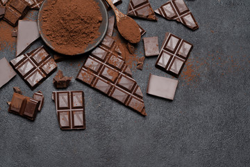 Dark or milk organic chocolate pieces and cocoa powder on dark concrete backgound