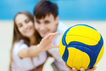 Young couple in love female girl and male man teenagers adults playing in volleyball with ball near water, river, lake at hot sunny summer day at sand beach. Summer hobbies leisure activities concept