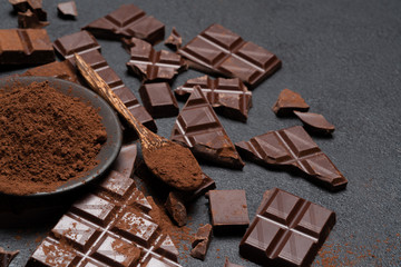 Dark or milk organic chocolate pieces and cocoa powder on dark concrete backgound