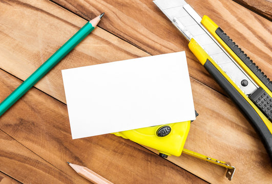 Blank business card with measuring tape tool, stationery knife and pencils on the table. Top view. Business template.