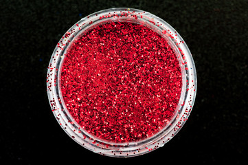 red sequins for manicure in a jar on a black background