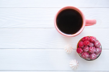A cup of black tea and tasty desserts, little merengues and fruit raspberry tart on white wooden table background, space for text.