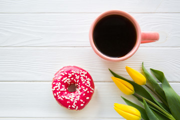 A cup of coffee, pink tasty doughnut and yellow tulip flowers, celebration concept. Birthday concept. Copy space for text, free space for text. 
