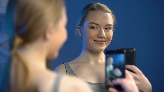 Playful teenager making faces, taking selfie by smartphone front of mirror