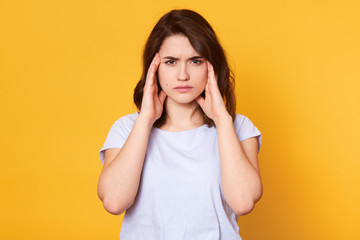 Woman with headache, has problem, lady standing with pain, keeps both hands on temples. Brunette...