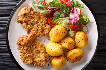 Fried pork steak in sesame breaded with new potatoes and salad closeup on a plate. horizontal top...